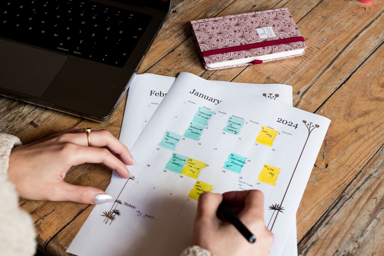 Hands checking and marking events on a 2024 calendar. Organized workspace theme.